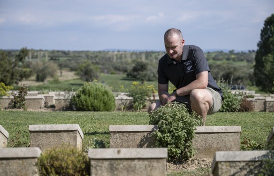 A male crouches alone paying his respects amongst gravestones in a cemetery.