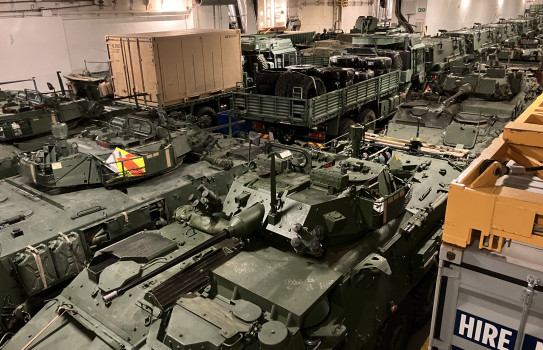 Large green military vehicles inside of what looks like a carpark, but is HMNZS Canterbury's cargo deck.