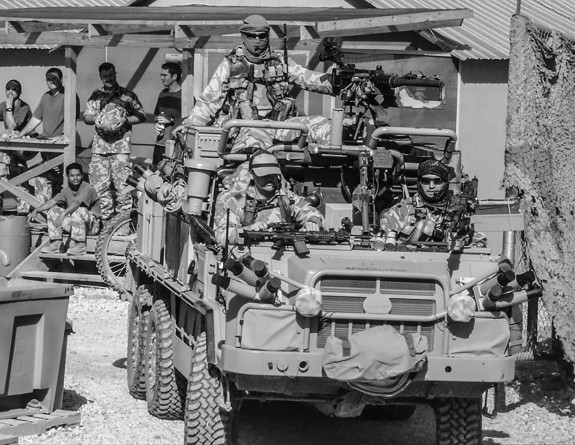 The image is black and white. NZSAS soldiers in Afghanistan on a military vehicle. All the people in the image are wearing uniform and carrying weapons.