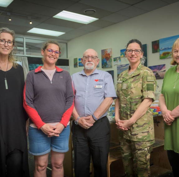 Five people smiling, some in casual clothes, others in camouflage uniform.