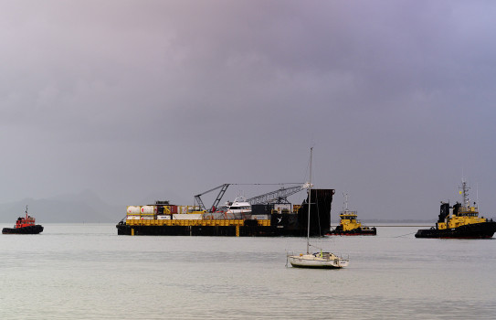 Three tugs and a barge on calm water in front of clouds.