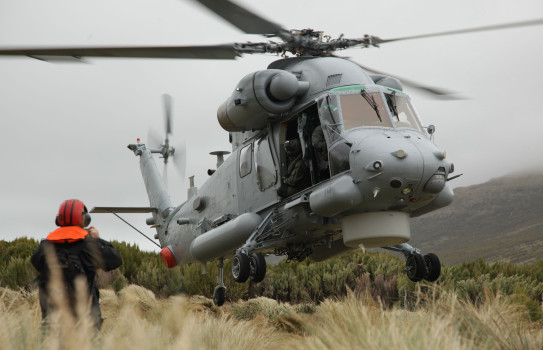 A Seasprite helicopter hovers about the ground as it comes to land. Someone is standing with their back to the camera in the bottomr left. 