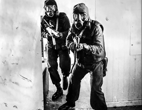 The image is black and white. Two soldiers come through a doorway, holding weapons and wearing masks.