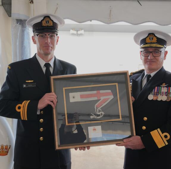 Two sailors both holding a frame, gifted to the outgoing commander at the ceremony underneath a large white tent.