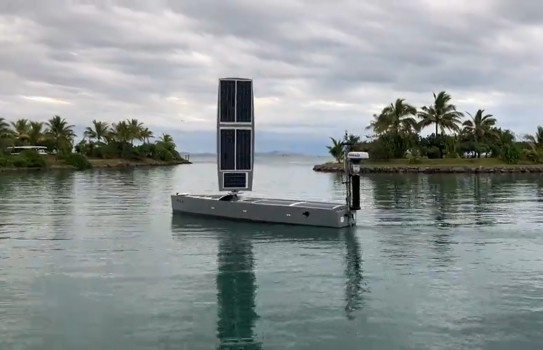 A small grey boat with a sail of solar panels operated in a harbour.