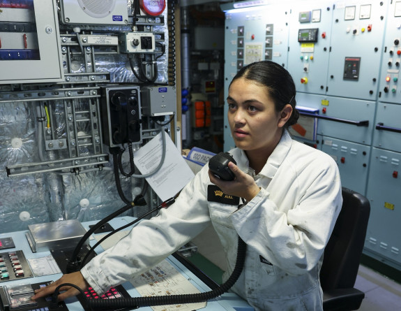 Sub Lieutenant Emily Aull uses a radio to communicate as she sits at a control panel, in a control room.