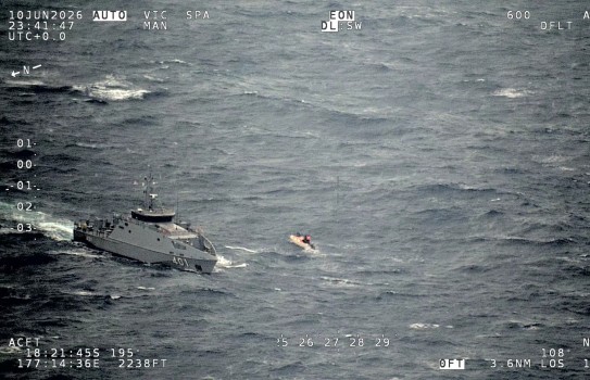 Photo from P-8A Poseidon of open ocean with a grey military ship and a much smaller orange civilian boat in choppy swells.