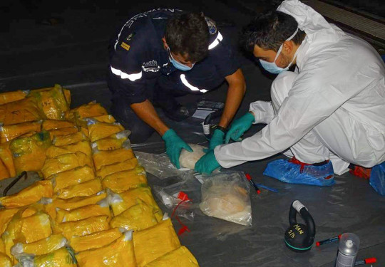 Multiple drug packages lined up on board French ship FS Floreal, as personnel expertly handle them in protective gear.