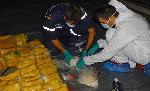 Multiple drug packages lined up on board French ship FS Floreal, as personnel expertly handle them in protective gear.