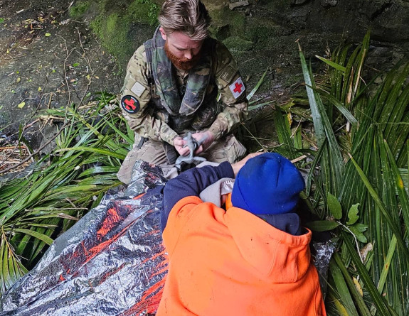 An Air Force Aviator with a someone from LandSAR work to support a patient before the winch