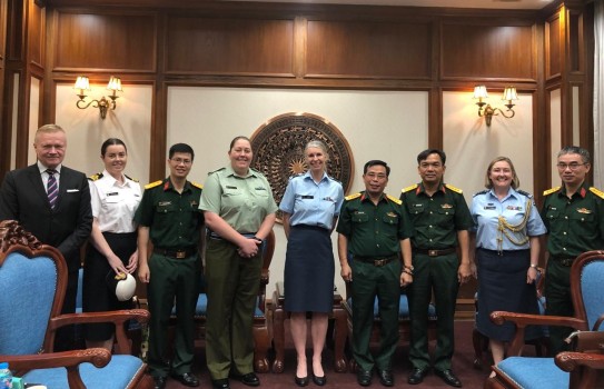 A group of military personnel standing inside, in a line. There is one person who is in a suit. 