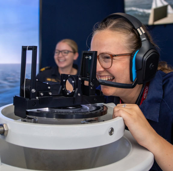 A woman wearing glasses and a headset smiles as she uses equipment in the ship bridge simulator at Devonport Naval Base.