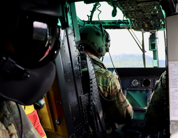 The cockpit of a Seasprite helicopter mid-flight with a crew member in the foreground wearing a helmet with a reflective visor.