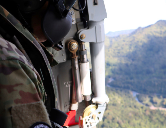 One of our personnel with a No.6 Squadron patch on their right arm, looks out of the open side door of the Seasprite while mid-flight.