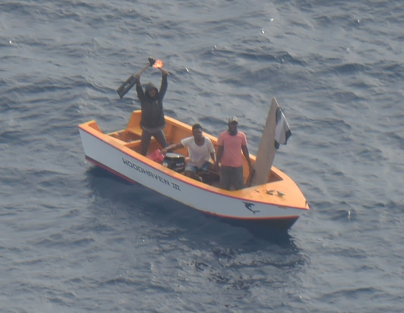 Three people wave for help whilst on a missing boat from Kiribati, photo taken from an RNZAF Orion.