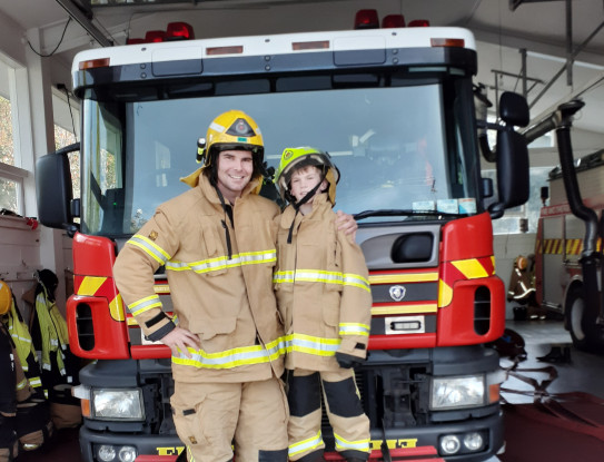 Lieutenant Jack Walters in his firefighter uniform, standing in front of a fire truck with his little buddy. 