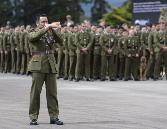 New Zealand Army soldiers stand in the background while a soldier blows a pūtātara