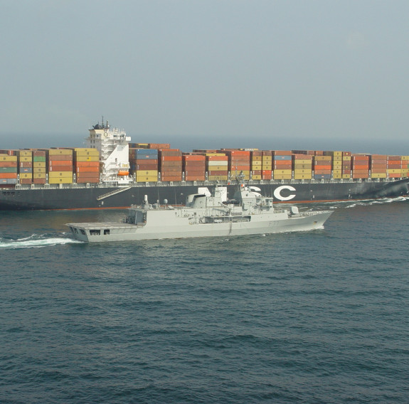 HMNZS Te Kaha escorts a large merchant vessel which has hundreds on containers on board.