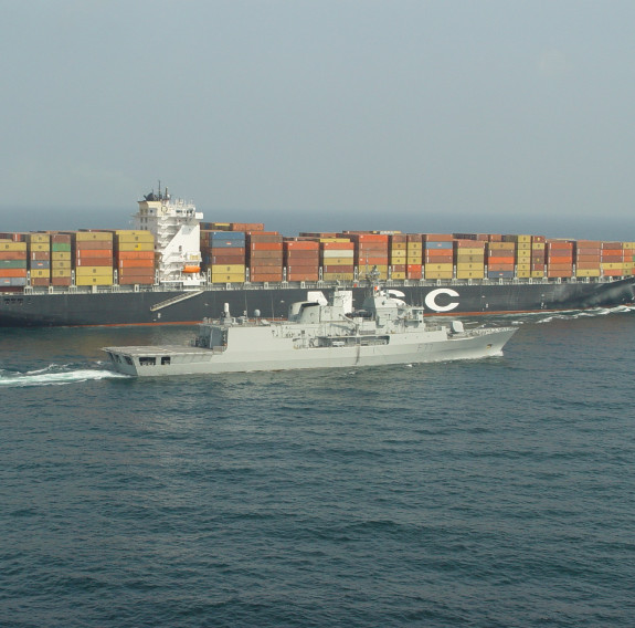 HMNZS Te Kaha escorts a large merchant vessel which has hundreds on containers on board.