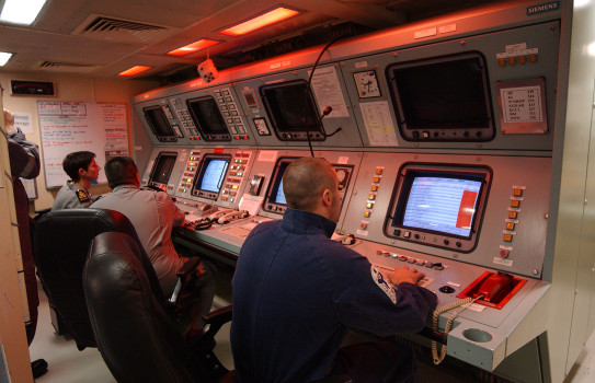 Three Navy crew sit in front of screens and a control panel within HMNZS Te Kaha.