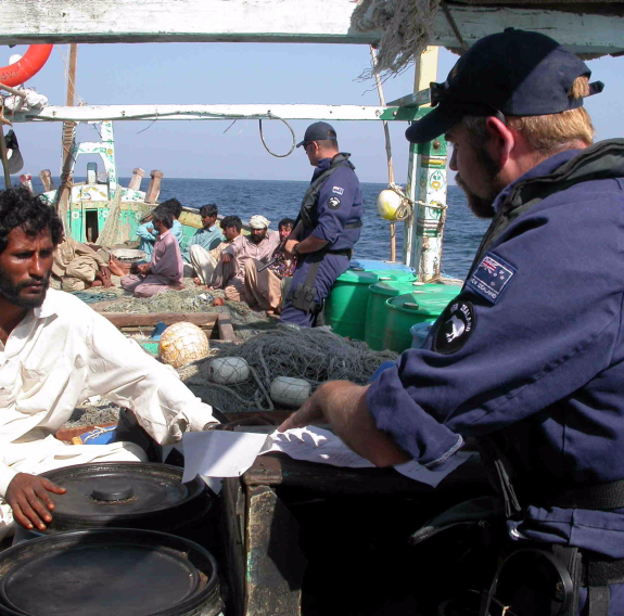 Boarding party personnel look over a vessel’s papers while the crew are positioned fo’ard.