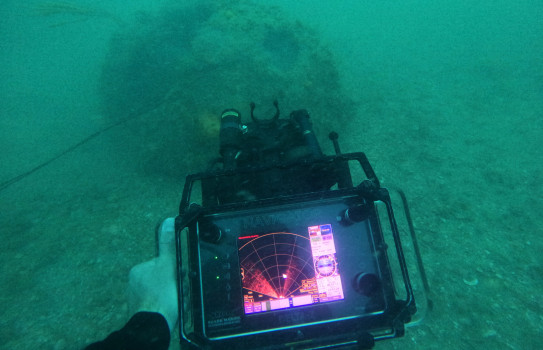 An underwater mine is scanned by a device that shows the mine on a radar-looking scanner.