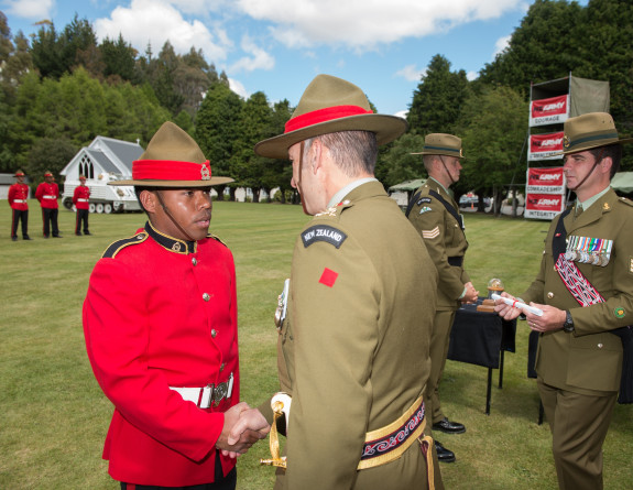 A soldier stands in uniform shaking the hand of another soldier in uniform (their back to the camera). 
