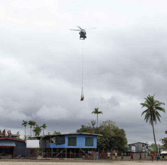 An NH90 helicopter with underslung cargo flies above buildings in Papua New Guinea.