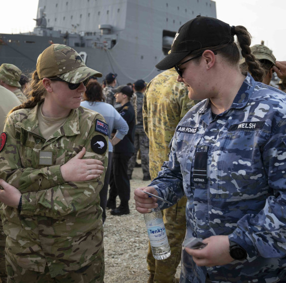 New Zealand and Australian personnel in military uniform mingle in front of a large grey ship.