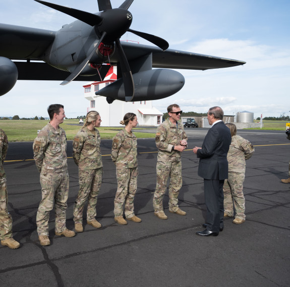 U.S. Ambassador Tom Udall (right) shakes the hands of USAF participants of Exercise Nocturnal Reach at RNZAF Base Auckland. The personnel are standing in a line on the tarmac under the wing of an aircraft.