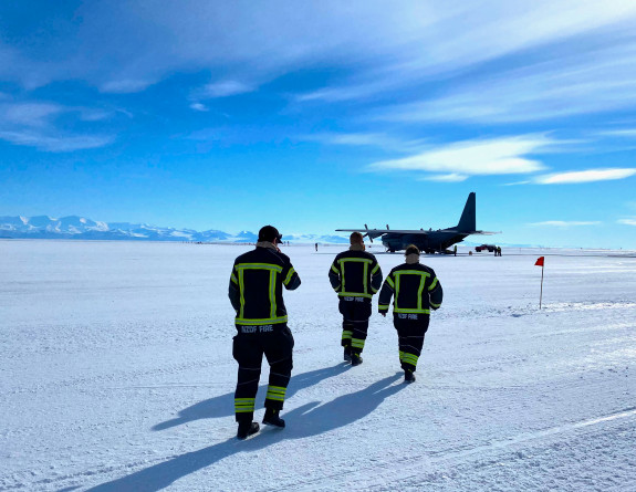 NZDF personnel in Antarctica, walking on the ice toward the Hercules aircraft. There is some cloud and blue sky.