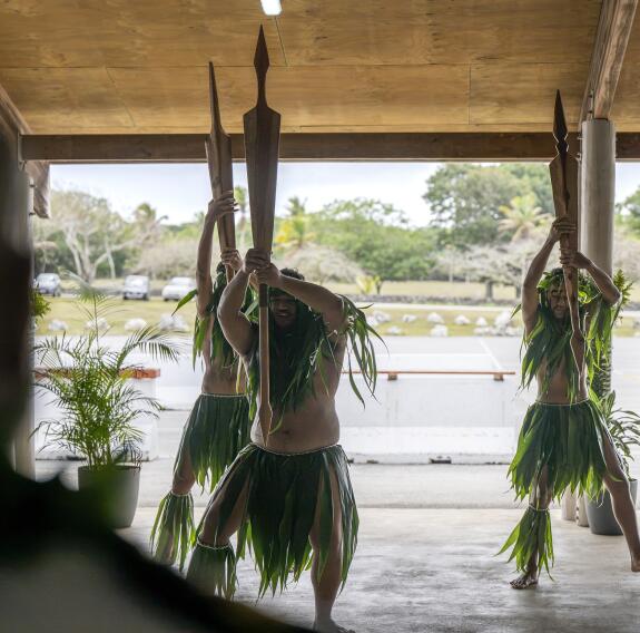 Three people in traditional dress hold up three large spears as part of a cultural performance.