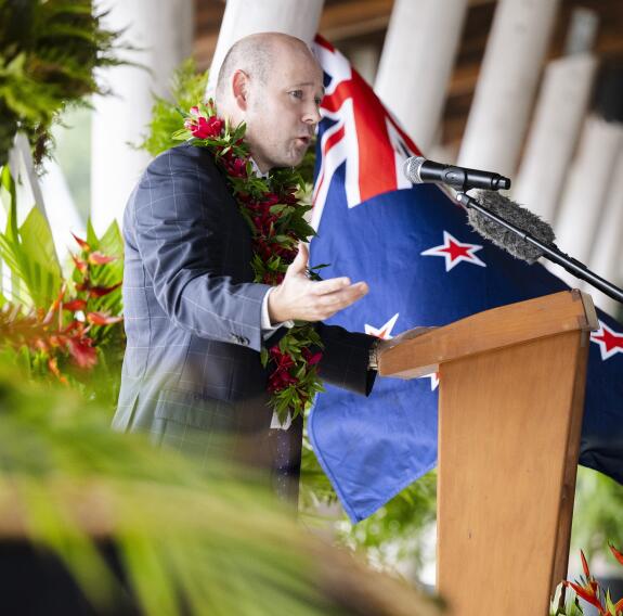 A man speaks at a podium in front of a New Zealand flag.
