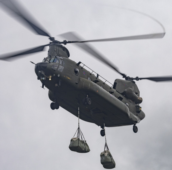 A low angle shot of a Royal Air Force Chinook helicopter as it lifts two large bags of chalk. 