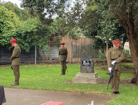 Soldiers in ceremonial dress stand guard around a headstone in 'lower on arms reverse' at a funeral in Otaki.