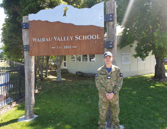 OCDT Anthony Raccoon was one of the 16 Air Force Cadets who supported staff and students at Wairau Valley School to build a community garden. Stands in front of the school sign on a sunny day. 