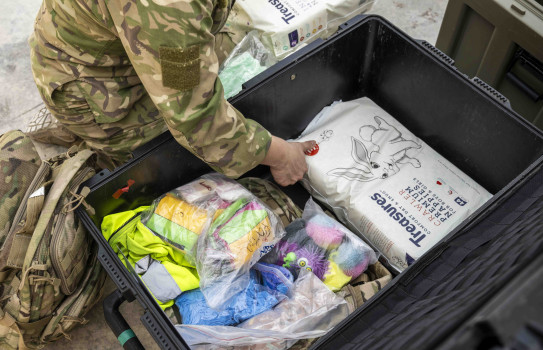 A soldiers hand moves a pack of nappies in a large crate amongst other essential supplies. 