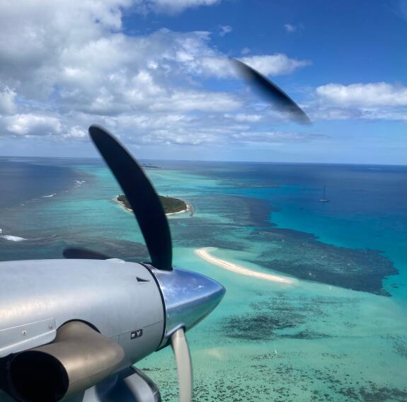 Propellor of an aircraft over Pacific Islands and reefs under scattered clouds and blue sky.