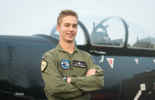 A man with blonde hair stands in front of the cockpit of a Texan aircraft.