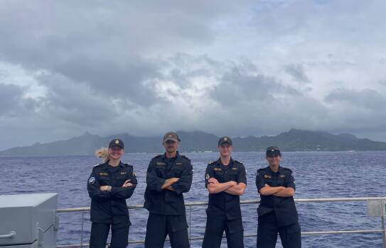 Four sailors standing on ship in the ocean. They have their arms crossed. 