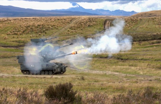 Three large tanks fire rounds in a field.