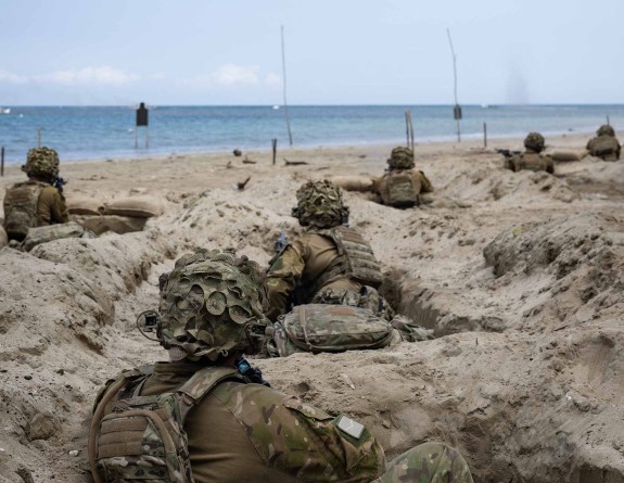 The image is taken from behind - only backs are seen. Soldiers simulated enemy beach assault including aerial and boat drones on Palawan Island, Philippines during Exercise Balikatan