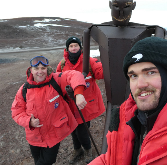 Three personnel standing next to a statue looking towards the camera.