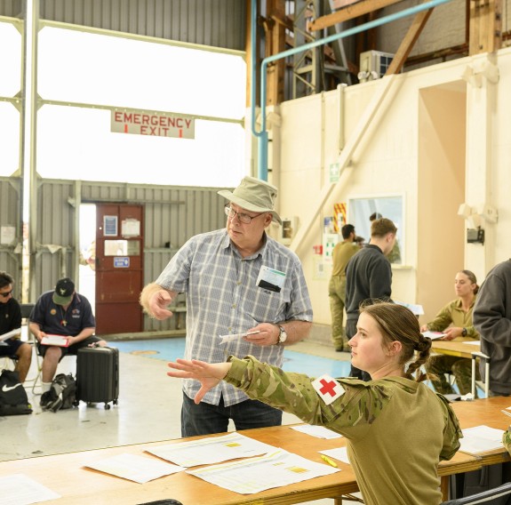 A medic gives instructions to a civilian in a hall, other people in the background are filling in forms.