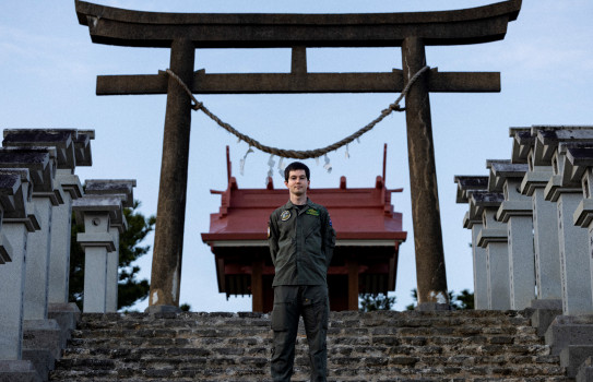An aviator stands on stairs in front of an archway.