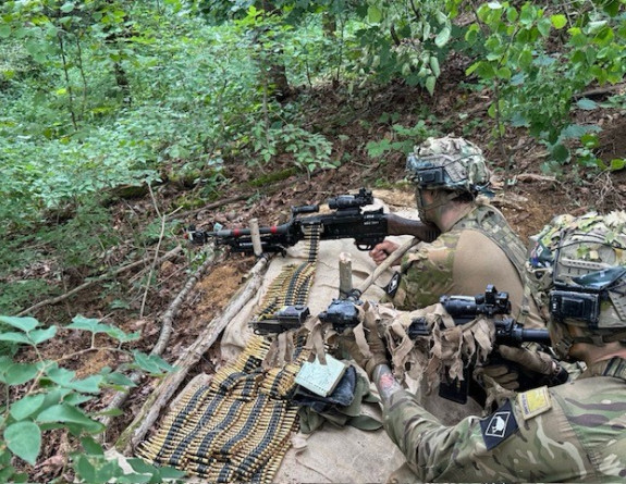 Soldiers lean their weapons on a sandbag in the bush.