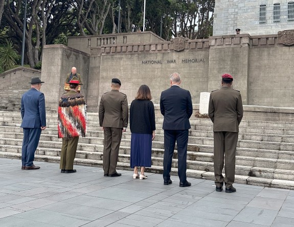 Six people, some in suits, some in Army uniform stand in front of a set or stairs at a war memorial.