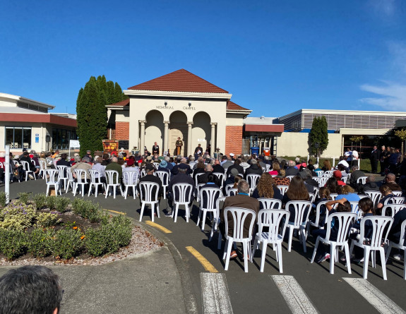 A crowd of people sitting on chairs - the photo is taken from behind looking towards a chapel service (help outside the chapel). 