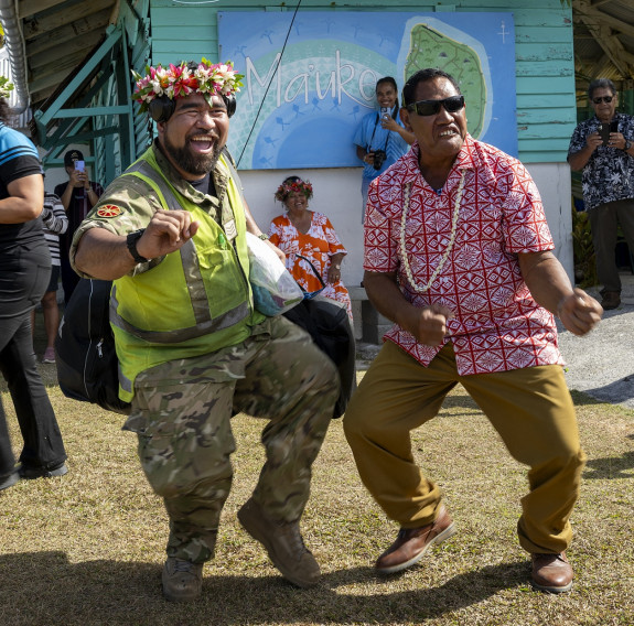 An aviator and a local person dance together with big smiles on their faces.
