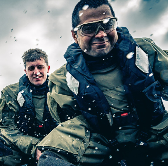 Three reserve force personnel, wearing life jackets get splashed while completing their training on the water.